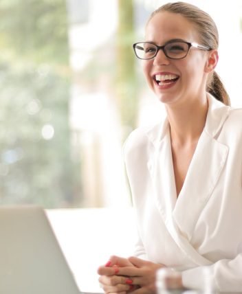 pexels-photo-3756679-3756679 Cheerful businesswoman in glasses working on a laptop, in a bright and modern office setting.
